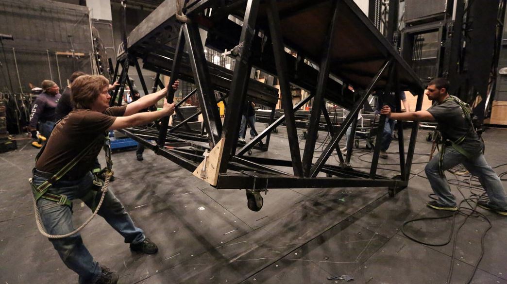A dim wing with rope locks, ladders, and labeled road cases in neat rows
