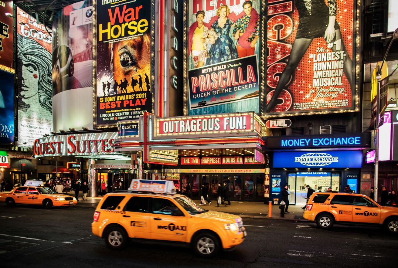 A marquee district sidewalk, load-in doors, and steel barricades set for a transfer